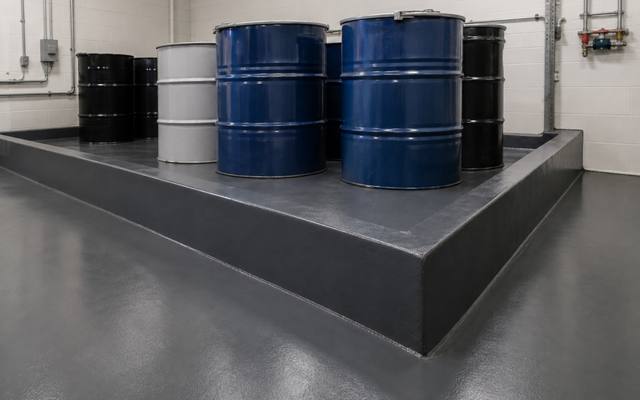 Bunded containment area holding drums on a dark chemical resistant floor with a coved upstand